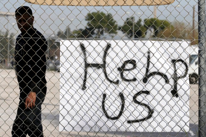 A migrant stands behind a banner at a former Olympic indoor stadium in Faliro, southern Athens, Monday, Dec. 14, 2015. Hundreds of people have been temporary housed in the stadium after being removed last week from Greece's northern border with Macedonia, which only allows Syrians, Afghans and Iraqis through on their trek to wealthier European countries - rejecting others as economic migrants who do not merit refugee protection. (AP Photo/Thanassis Stavrakis)