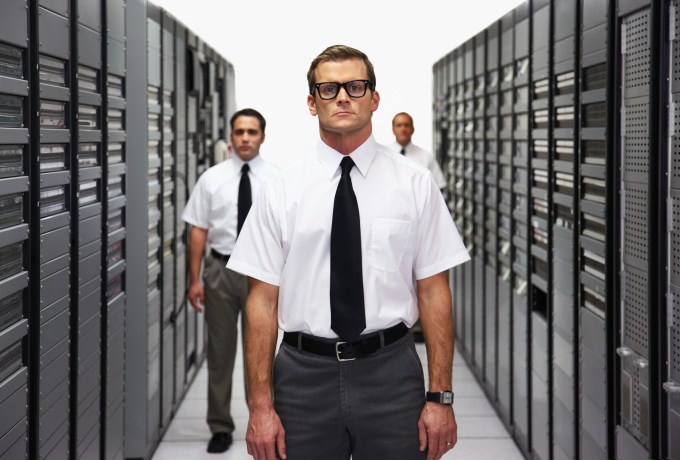 Male IT workers standing at attention between computer servers